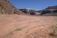 a dirt road through a desert plain with a mountain behind it and a clear blue sky in the background