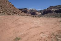 a dirt road through a desert plain with a mountain behind it and a clear blue sky in the background