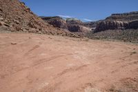 a dirt road through a desert plain with a mountain behind it and a clear blue sky in the background