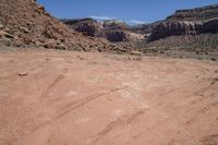 a dirt road through a desert plain with a mountain behind it and a clear blue sky in the background