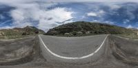 an empty roadway near a steep hill and blue sky with clouds in the background at the top