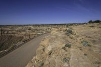 a winding paved dirt road near a wide open area of rocks and mountains with fencing