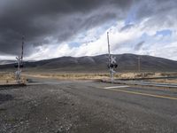 road with a railroad crossing in front of a mountain range with dark clouds in the background