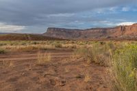 dirt road leading towards distant red cliffs and desert area in background with blue sky and clouds