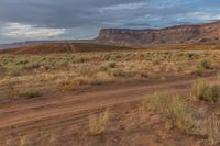 dirt road leading towards distant red cliffs and desert area in background with blue sky and clouds