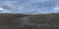 view of a large open area with a hill in the background, clouds are floating over