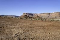 a view of a mountains range with sparse grass in the foreground and a dirt plain out front