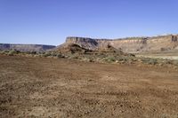 a view of a mountains range with sparse grass in the foreground and a dirt plain out front