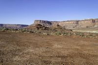 a view of a mountains range with sparse grass in the foreground and a dirt plain out front