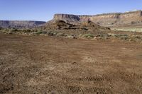 a view of a mountains range with sparse grass in the foreground and a dirt plain out front