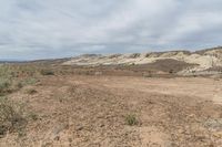 an area with very no grass in the middle and mountains in the distance, some of which have some bushes around it