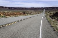 a lonely highway with an arrow painted on it and bushes growing out of the pavement