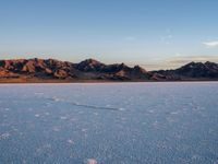 a vast open area with the mountains in the background and footprints across it at sunset