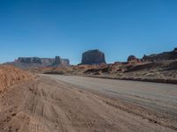 a long desert road leading through desert mountains and desert land in the background with dirt ground and rocks