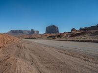 a long desert road leading through desert mountains and desert land in the background with dirt ground and rocks