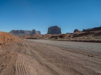 a long desert road leading through desert mountains and desert land in the background with dirt ground and rocks