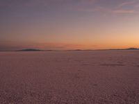 two people riding on the back of a motorcycle at sunset on a flat, barren field