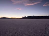 a lone motorcycle sitting in the middle of a vast plain area at dusk with mountains