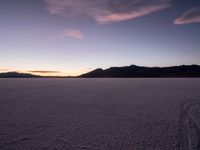 a lone motorcycle sitting in the middle of a vast plain area at dusk with mountains