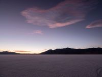 a lone motorcycle sitting in the middle of a vast plain area at dusk with mountains