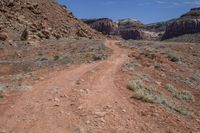 a dirt road through a desert plain with a mountain behind it and a clear blue sky in the background