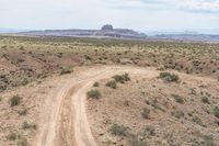 a dirt road in the middle of an arid area with mountains in the distance and small scrub covered hills near