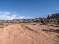 dirt road through the desert in the distance with blue sky above and white clouds in distance