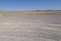 an area with a dirt field, sand and water on the horizon is dry grass