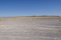 an area with a dirt field, sand and water on the horizon is dry grass