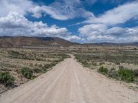 a long dirt road leading up to a mountain range, in the distance, and there is a blue sky and white cloud