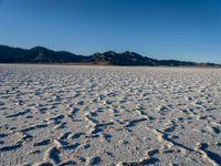 an open salt desert with sparse snow on it and mountains in the distance under blue sky