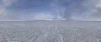 an open empty snow field under cloudy skies with mountains in the background and clouds covering mountains