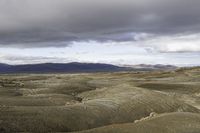 an image of a desert scene with mountains in the background under a cloudy sky with white clouds