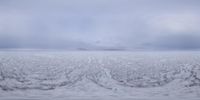 an empty snowy landscape with mountains in the distance and a lone cloud in the sky