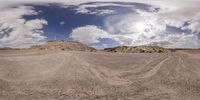 the panoramic image shows an empty field with rock formations in the background and clouds