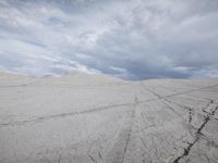 an empty dirt road runs along a vast plain with some clouds overhead and sparse scrub like rocks