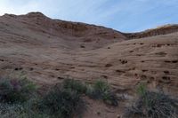 an empty bench sits on the edge of a cliff in red desert with brown rocks, and green shrubs and brush