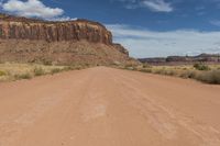 a red dirt road passing through a desert with lots of tall cliffs in the background