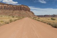 a red dirt road passing through a desert with lots of tall cliffs in the background