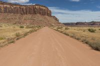 a red dirt road passing through a desert with lots of tall cliffs in the background