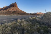 a paved roadway with a red mountain behind it in the background and some grass on both sides