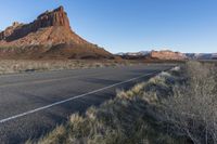 a paved roadway with a red mountain behind it in the background and some grass on both sides