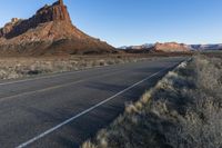 a paved roadway with a red mountain behind it in the background and some grass on both sides