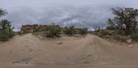 dirt road leading to some hills and plants on a cloudy day in the desert with storm clouds overhead