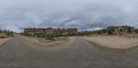 a wide angle view of a road and a dirt field with some buildings near by