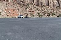 two vehicles driving on a mountain side road in the desert area of a large mountainous area