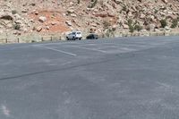 two vehicles driving on a mountain side road in the desert area of a large mountainous area