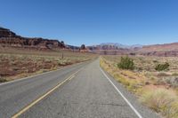 a highway winds through desert scenery with mountains in the background and blue sky above it