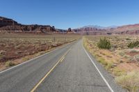 a highway winds through desert scenery with mountains in the background and blue sky above it