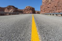 a yellow line on the highway in front of red mountain mountains and a bright blue sky